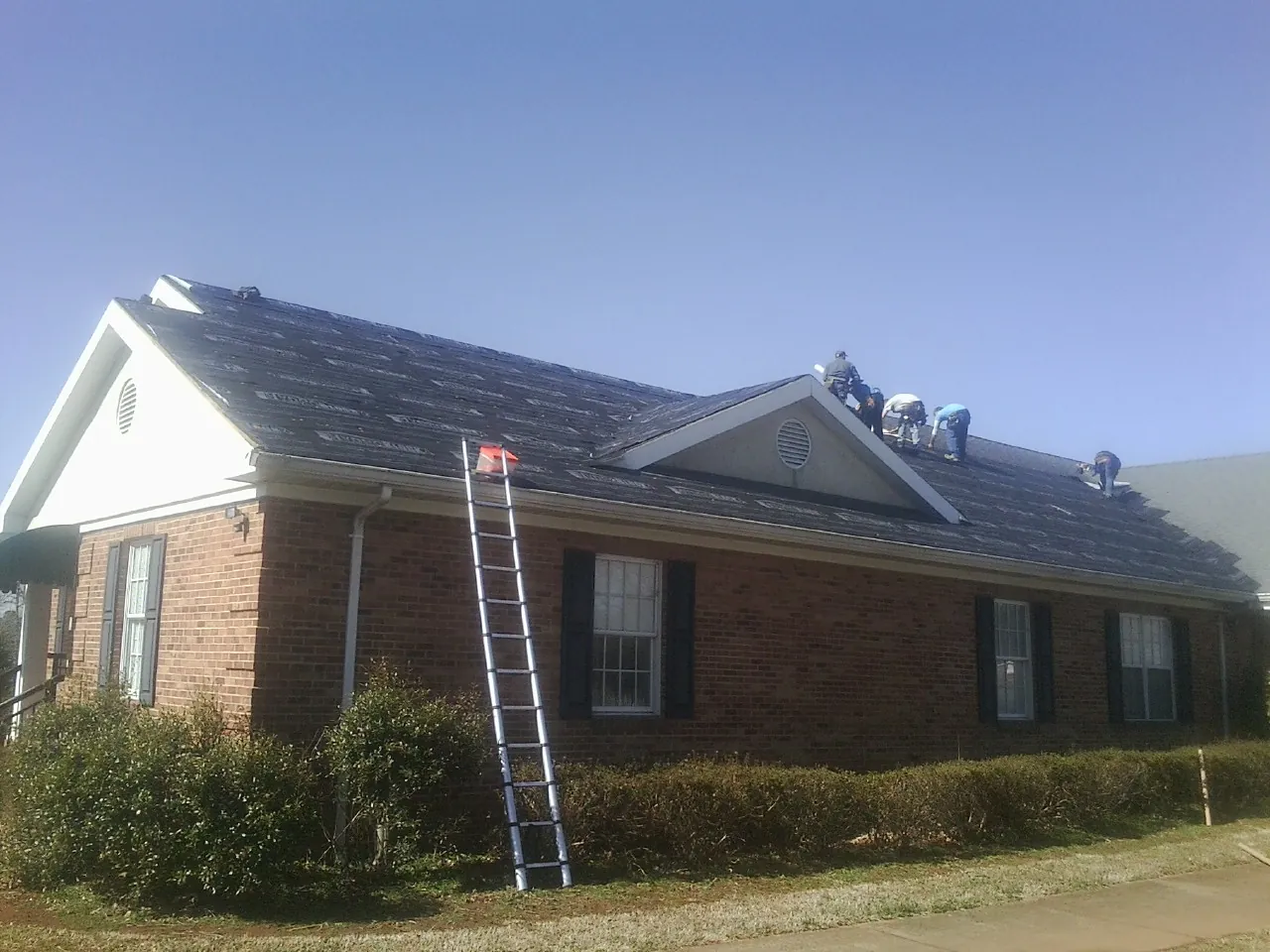 Crew tearing shingles off a brick ranch roof with a ladder set — Metal Roof Repair work by our crew in Ola