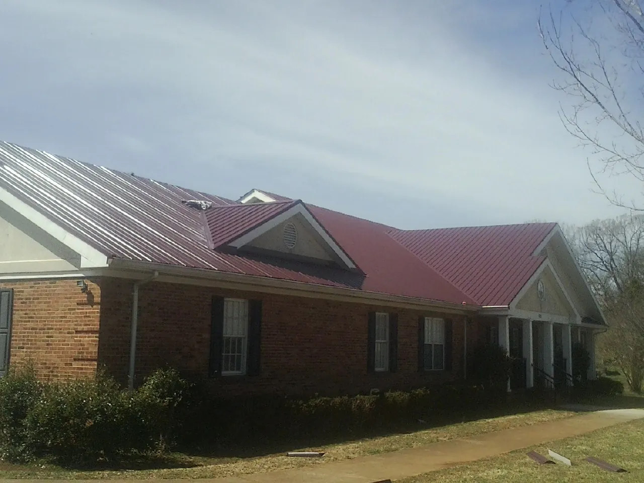 Red metal roof with gabled entries on a long brick building, from a Hail Damage Roof Repair job in Ola