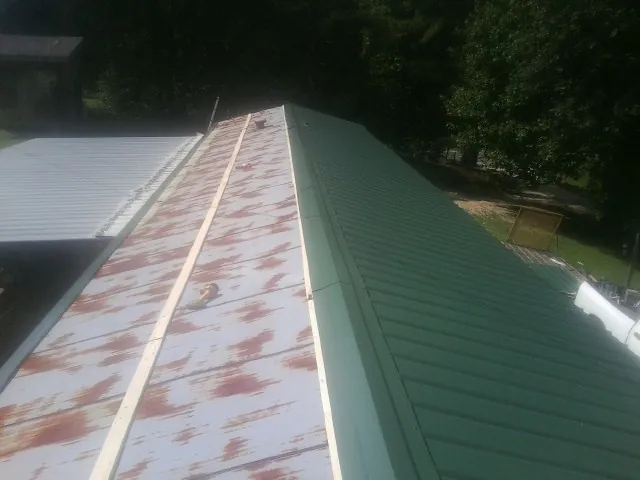 Old rusted panels beside newly installed green metal roofing — Wind Damage Roof Repair by Roofing Brothers in Ola