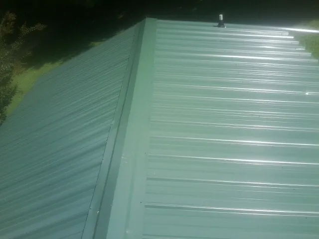 New green metal panels meeting at the ridge of a roof — Flat Roof Repair work by our crew in Ola