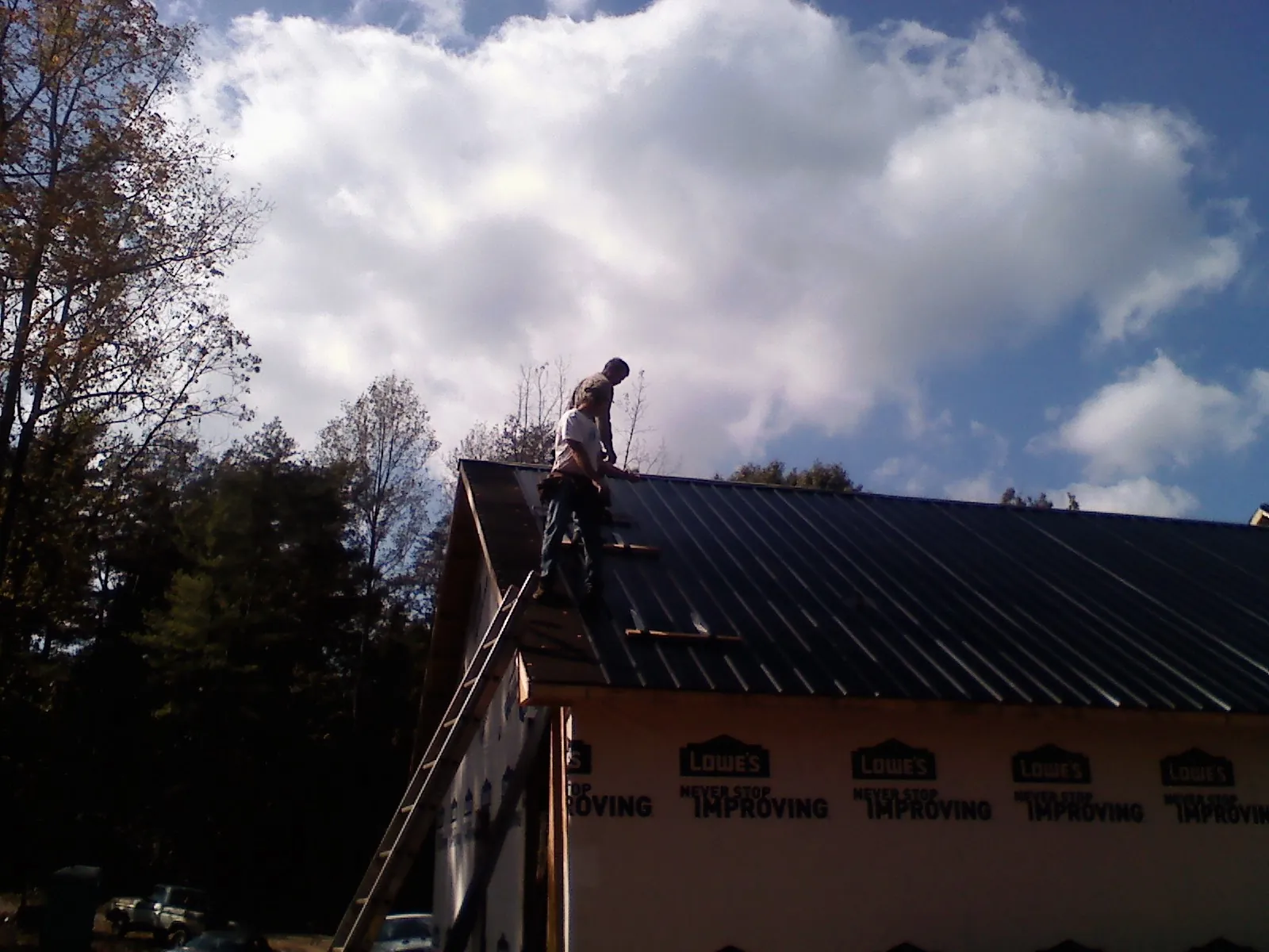 Roofer fastening dark metal panels high against a cloudy sky, from a Roof Inspection job in Ola