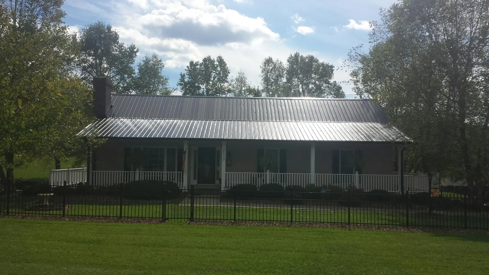 Gray metal roof on a brick ranch with a full width front porch — Gutter Guard Installation work by our crew in Ola