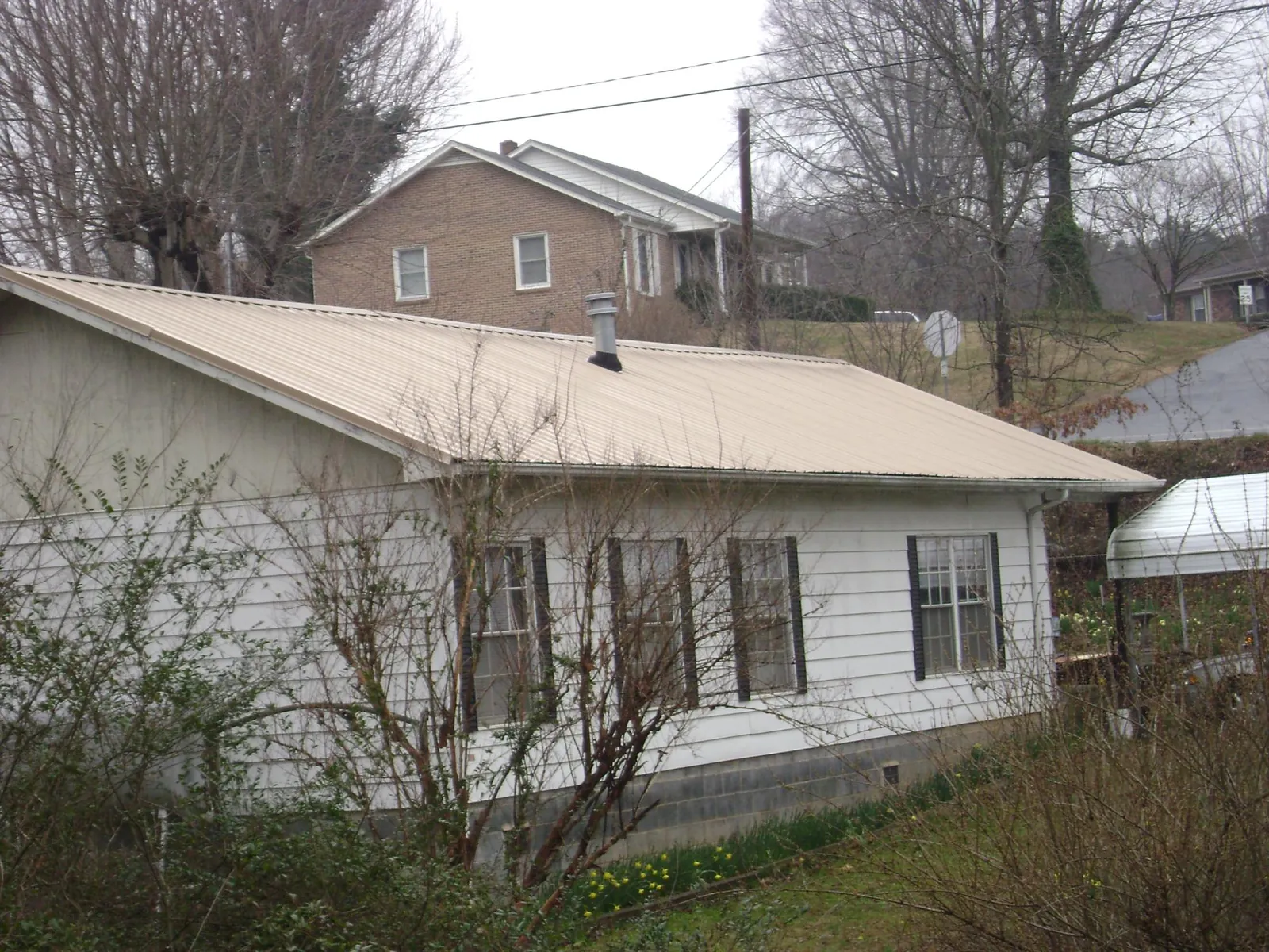 Tan metal roof on a white sided house set into a hillside — Commercial Roofing by Roofing Brothers in Ola