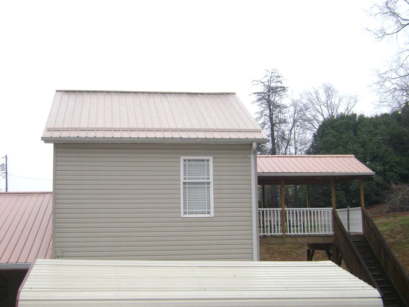 Tan metal roofs on a two story addition and attached porch, from a Roof Replacement job in Ola